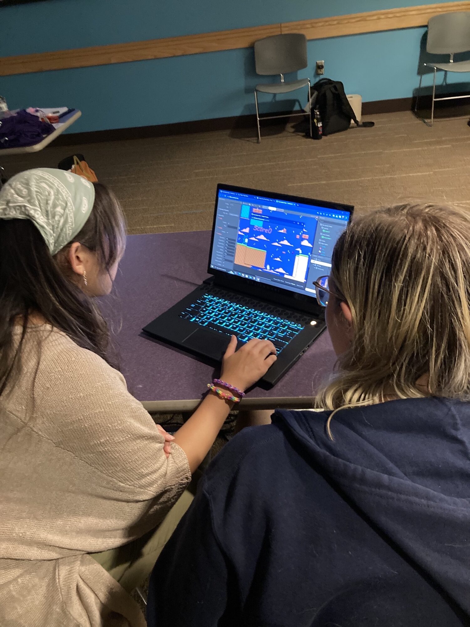 two girls sitting at a computer, working on making a video game