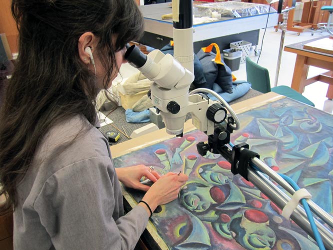 A picture of a Conservator cleaning a painting under magnification.  